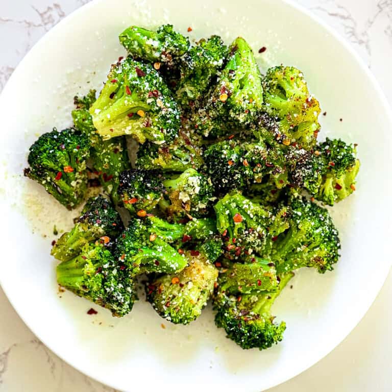 air fryer frozen broccoli - feature image. Broccoli on a white plate sprinkled with parmesan cheese and red pepper flakes