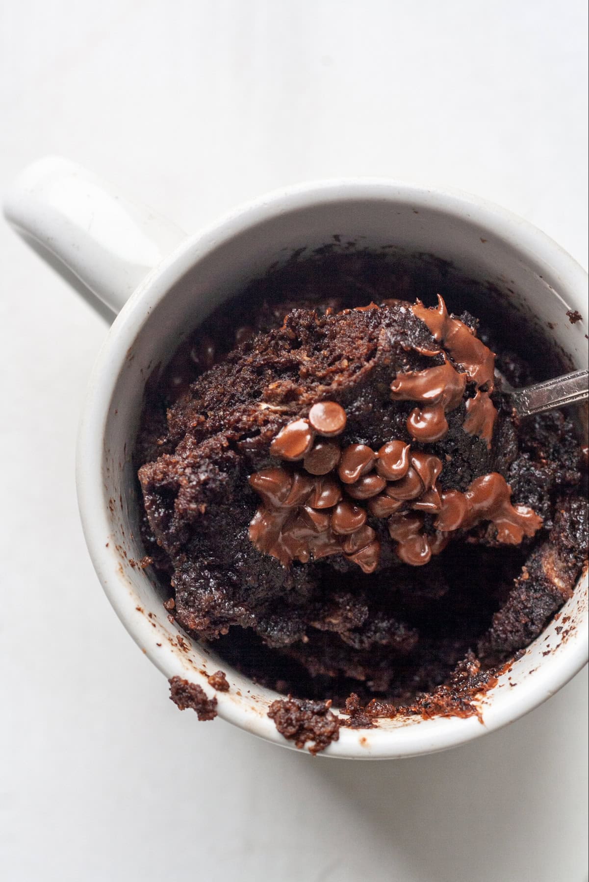 Spoonful of chocolate chip mug cake  in a white mug sprinkled with dairy free chocolate chips on top