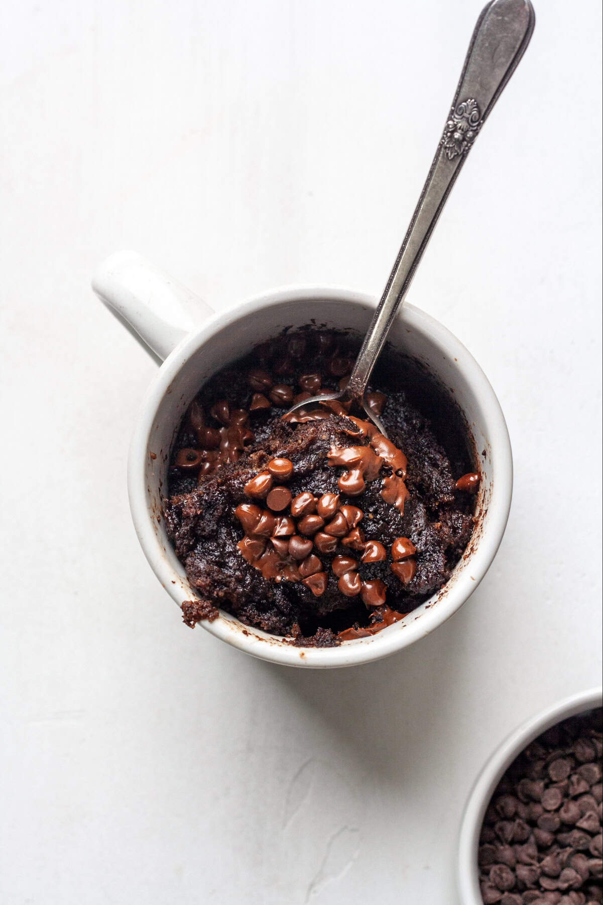 Double Chocolate Chip Mug Cake in a white cup with a spoon of cake and chocolate chips on the side for aesthetic