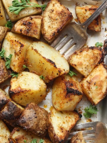 seasoned potatoes feature image on a baking pan with a fork cutting into a potato cube