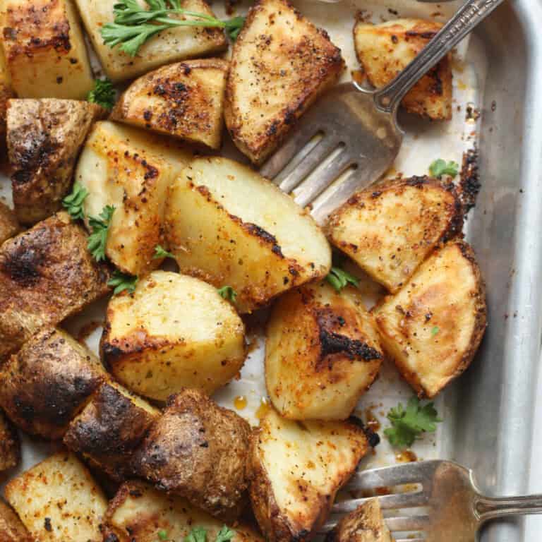 seasoned potatoes feature image on a baking pan with a fork cutting into a potato cube