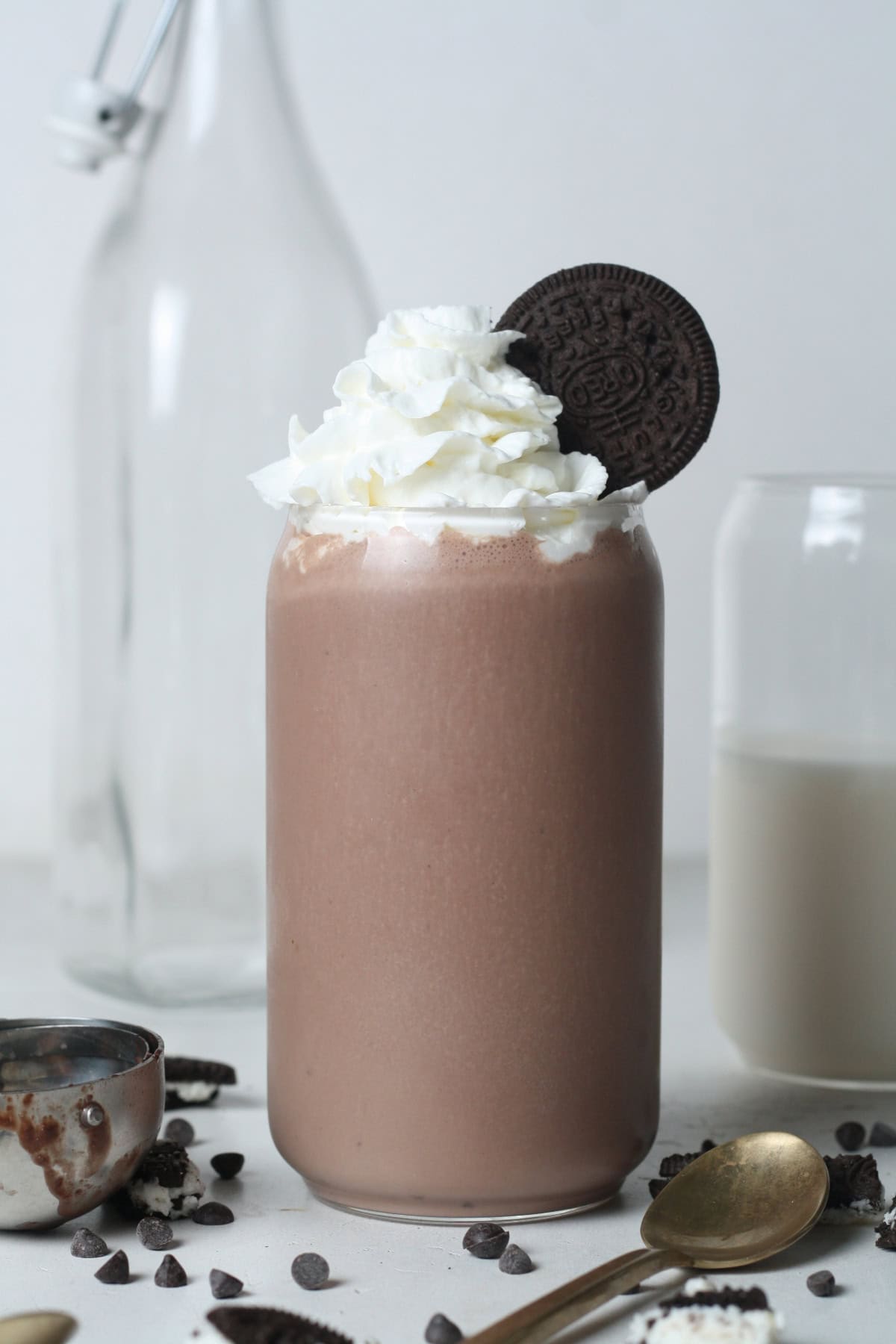 Profile view of a vegan Oreo protein shake in a glass topped with dairy-free whipped cream and an Oreo on the side for presentation