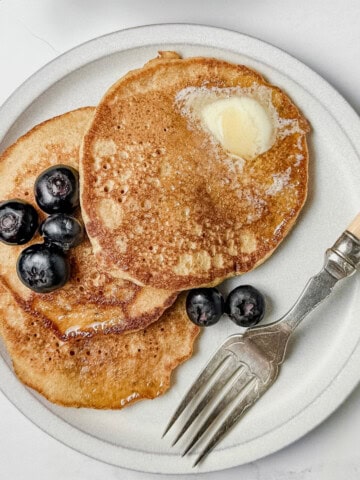 Dairy Free Pancakes served with sliced butter and blueberries on top in a plate with a fork on the side