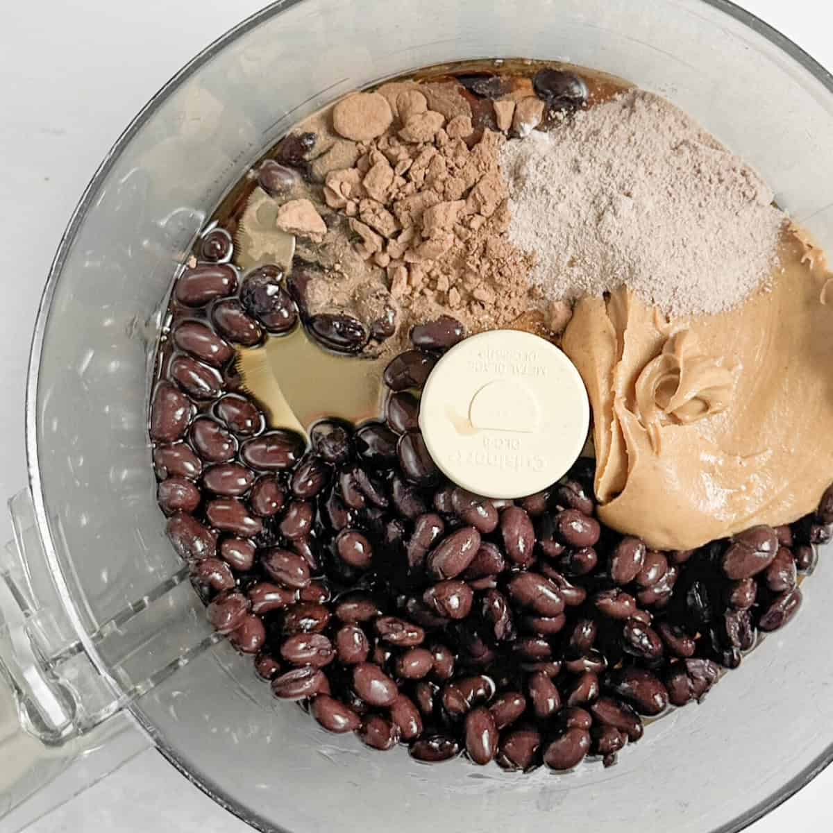 ingredients including black beans, nut butter, protein powder in a blend