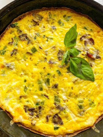 Veggie Loaded Frittata in the pan with basil leaf as garnish