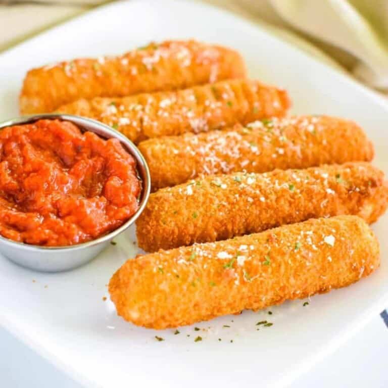 air fryer frozen mozzarella sticks in a white plate with dipping sauce on the side