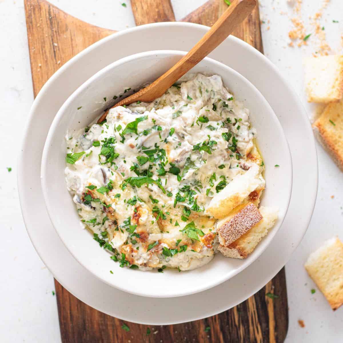 Creamy Mushroom Dip - white bowl with a wooden spoon and toasted bread on side.