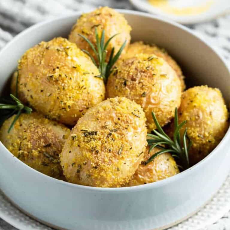 Close-up view of whole roasted baby potatoes with herbs in a white bowl