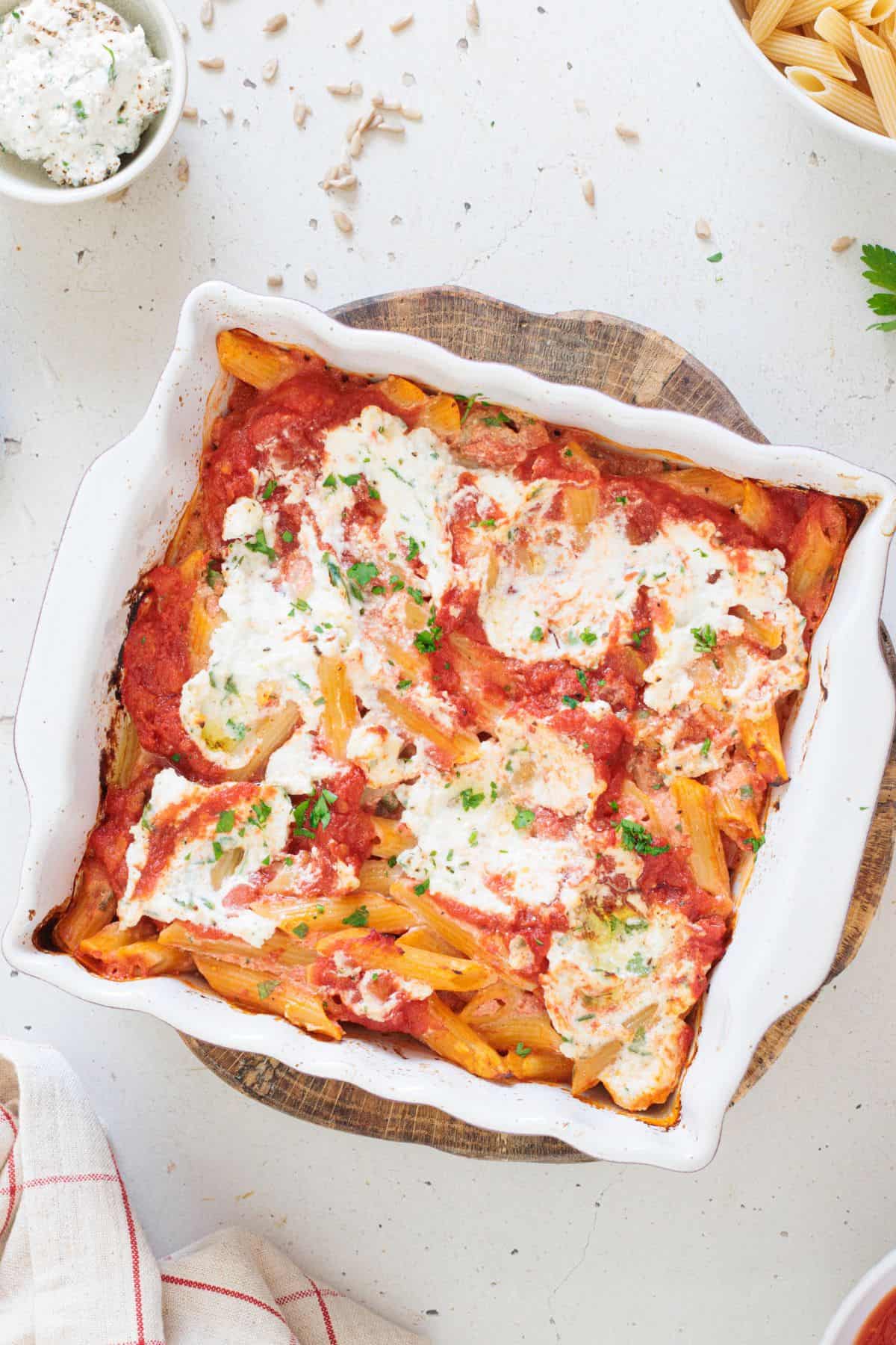 overhead shotof vegan baked ziti served in a casserole baking pan garnished with parsley on top - main image