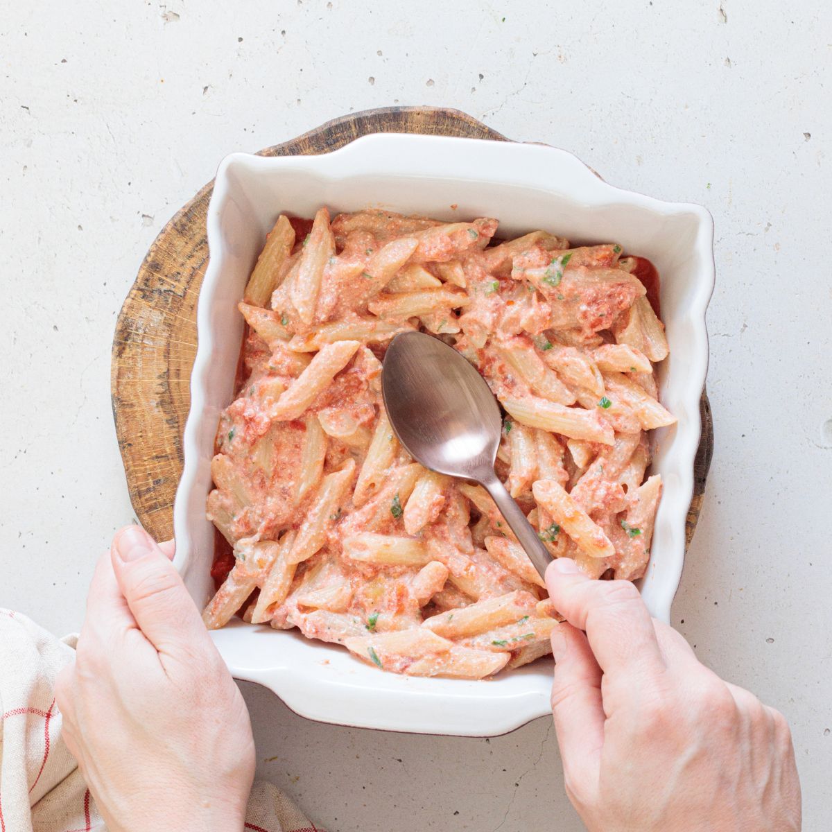 spreading the vegan ziti mixture in casserole dish before topping with cheese and sauce.
