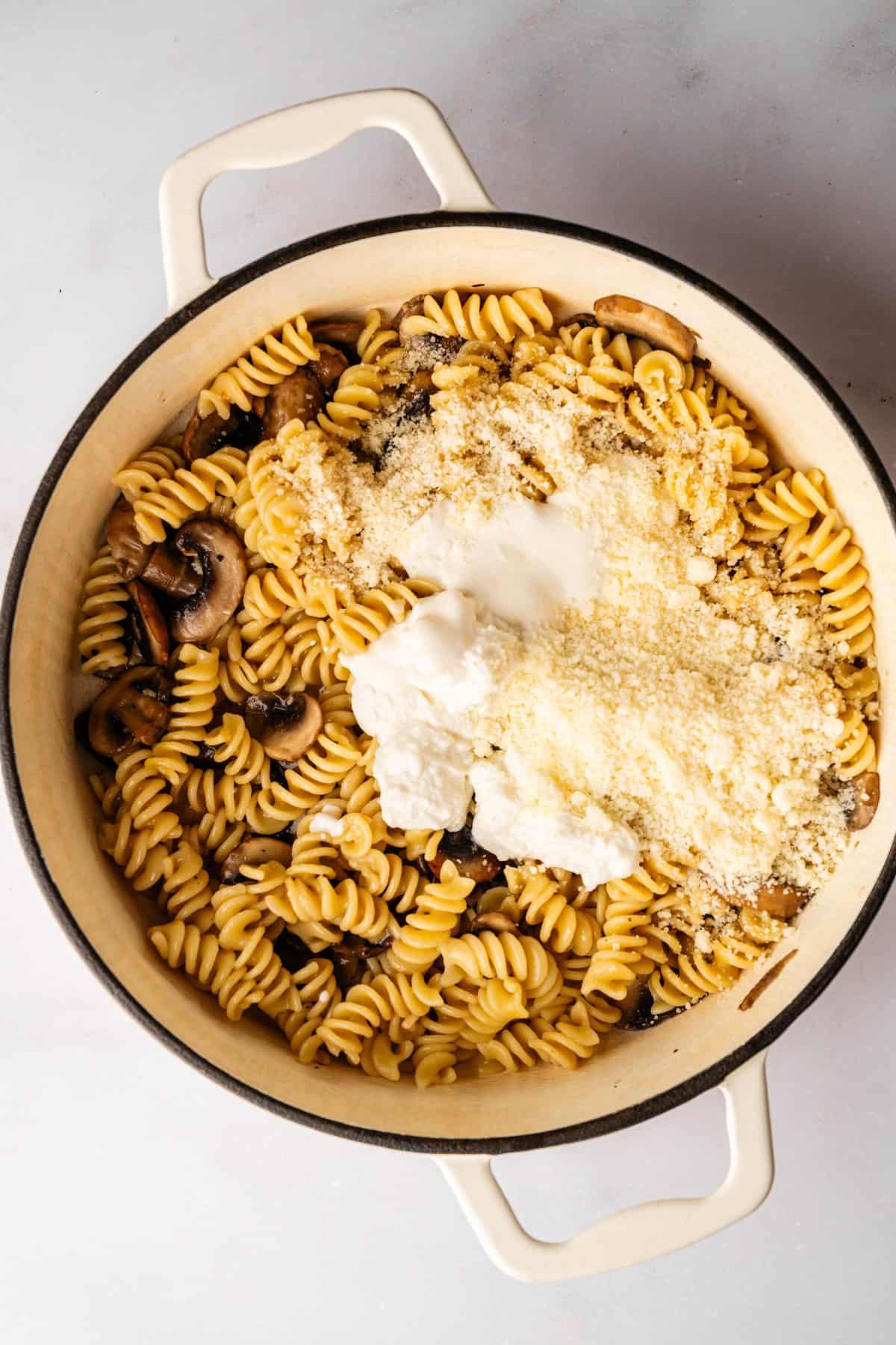 Adding ricotta cheese and Parmesan over cooked mushroom pasta in a pot