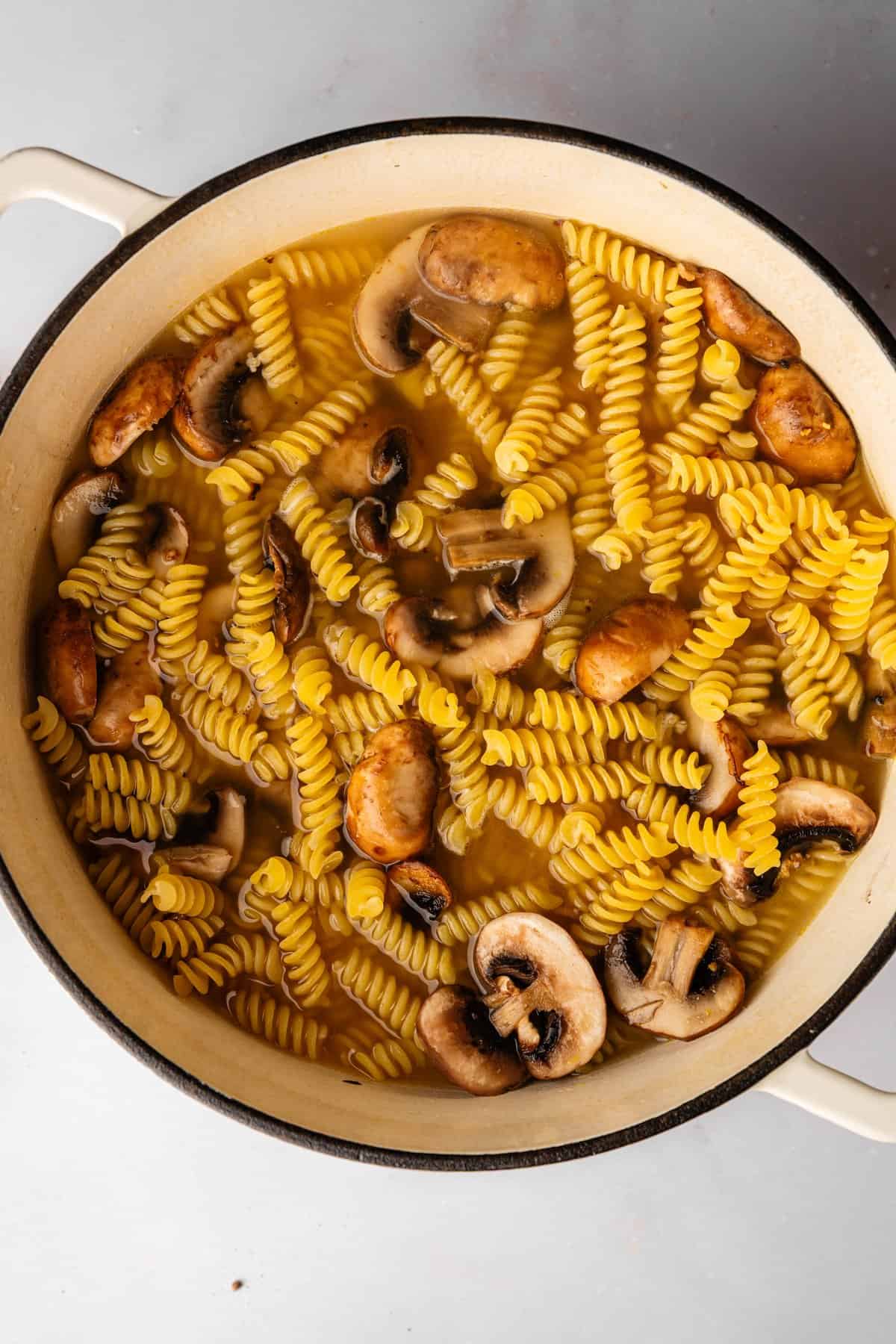 Fusilli pasta and mushrooms simmering in vegetable broth in one pot