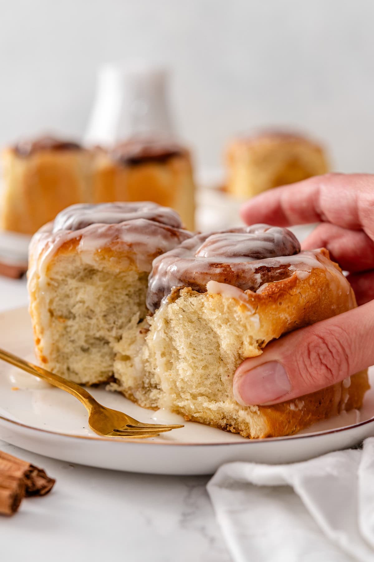 A hand pulling apart a soft vegan cinnamon roll on a plate, showing the pull-apart texture and stretchy crumb