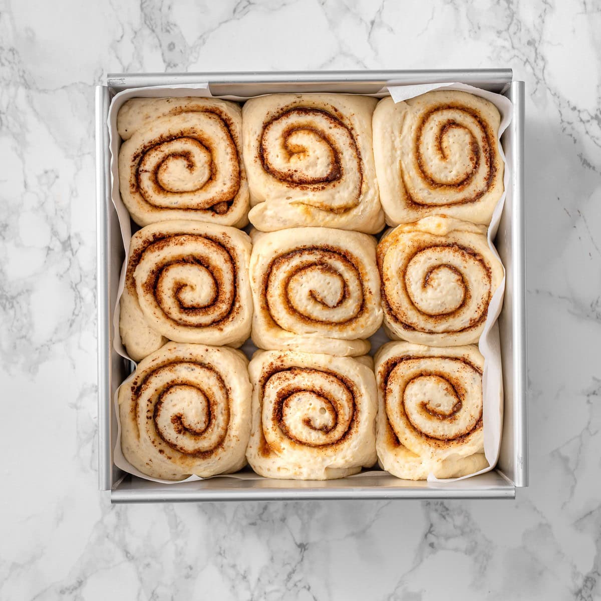 Proofed vegan cinnamon rolls in the baking pan after the second rise, puffed up and pressing against each other, ready for the oven