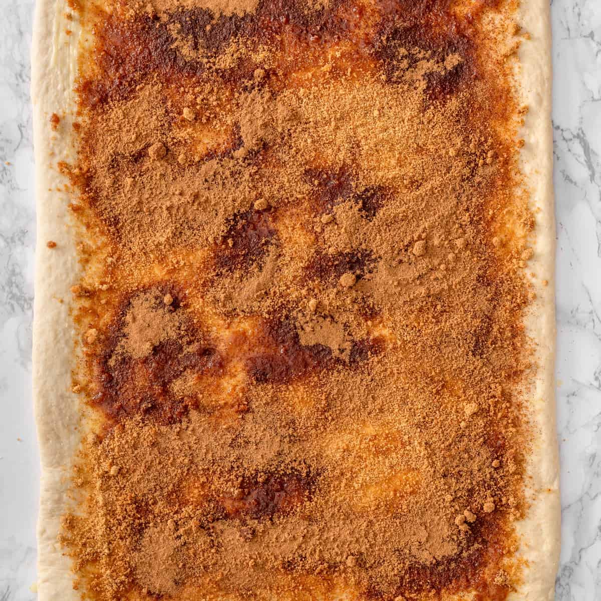 Rolled-out dough covered with a thick layer of cinnamon sugar and brown sugar filling, ready to be rolled up into a log
