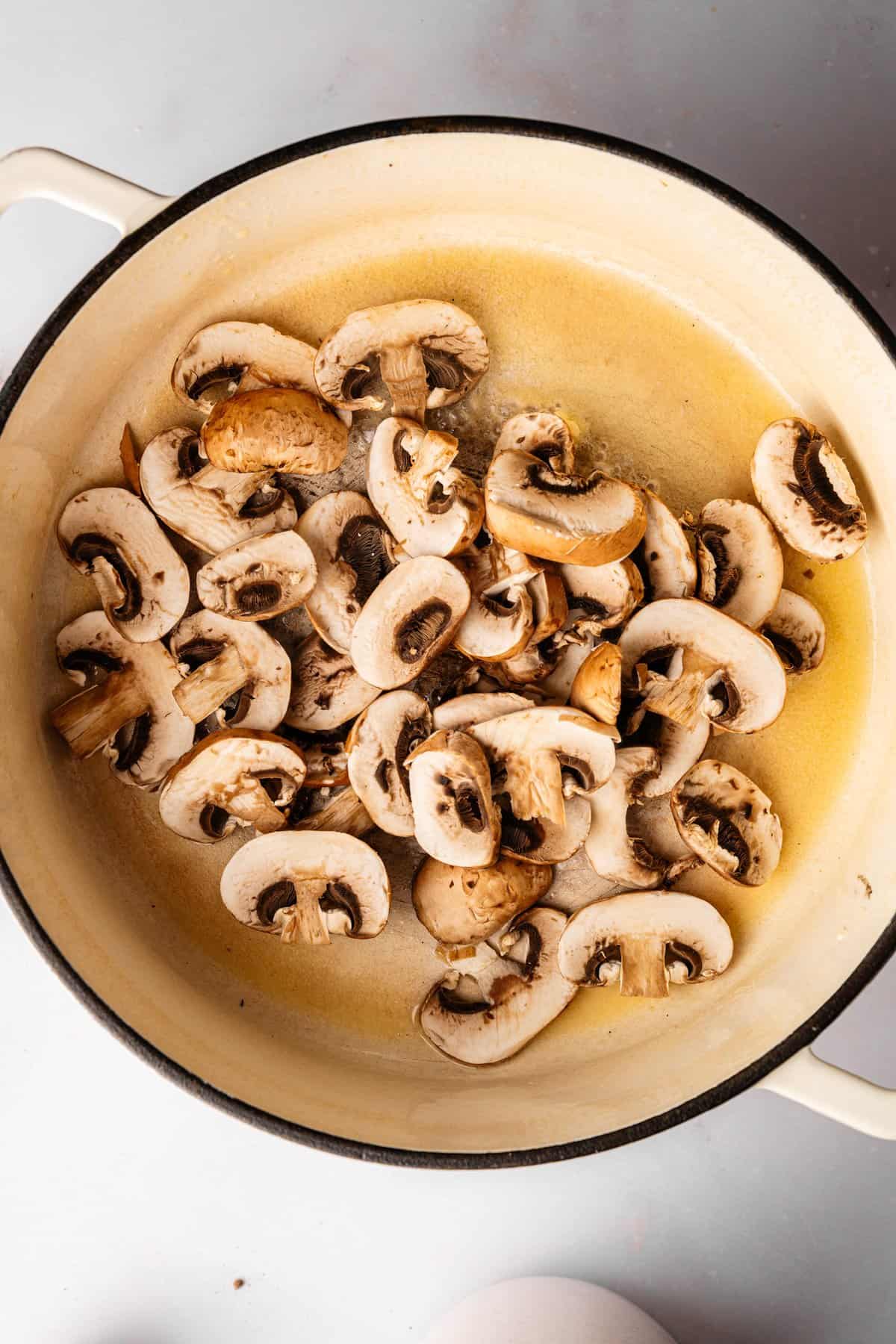 Sliced portobello mushrooms saut&eacute;ing in butter and garlic in a Dutch oven