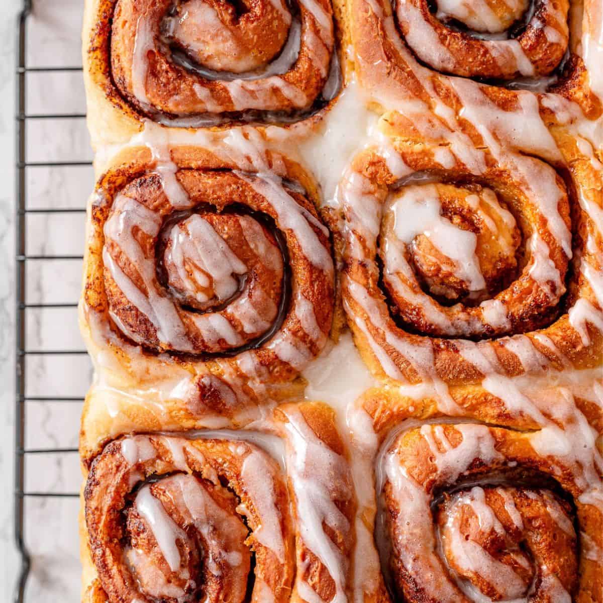 Vegan Cinnamon Rolls on a cooling wire rack topped with vanilla glaze