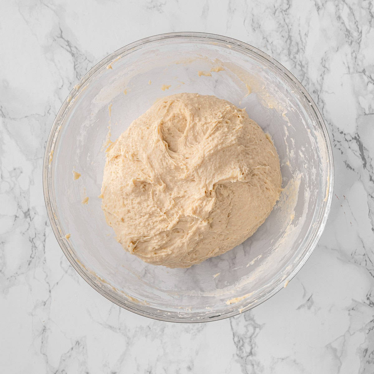 Vegan cinnamon roll dough in a glass bowl after initial mixing, showing a shaggy, just-combined texture before kneading