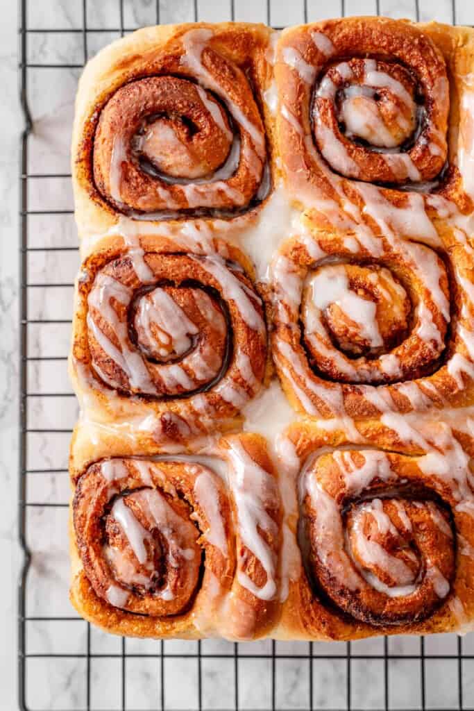 Close-up overhead of vegan cinnamon rolls on a wire rack, highlighting the beautiful cinnamon sugar swirl pattern with a drizzle of vanilla glaze