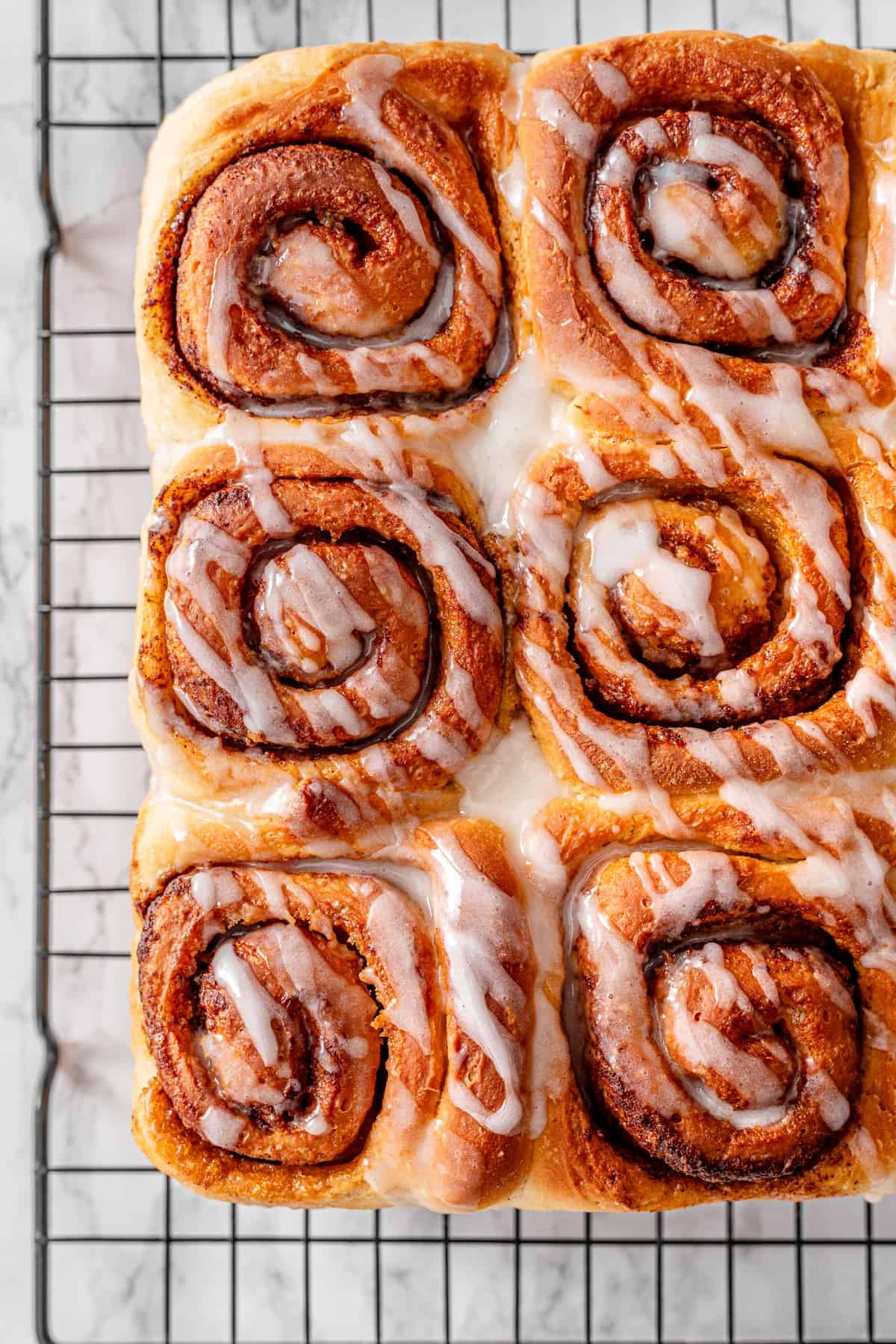 Close-up overhead of vegan cinnamon rolls on a wire rack, highlighting the beautiful cinnamon sugar swirl pattern with a drizzle of vanilla glaze