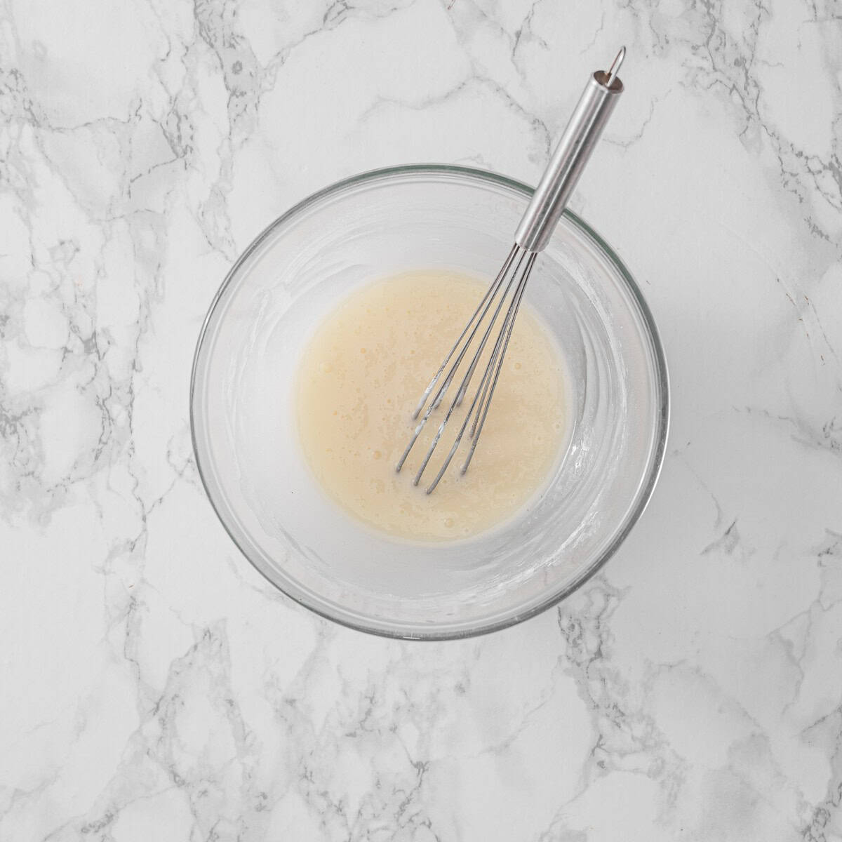 Smooth, pourable vanilla glaze whisked together in a glass bowl with a small whisk, ready to drizzle over the cinnamon rolls