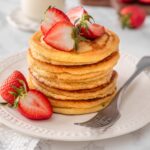 Chickpea Flour Pancakes served and ready to eat topped with strawberries and a fork on a white plate.
