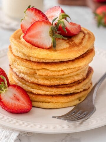Chickpea Flour Pancakes served and ready to eat topped with strawberries and a fork on a white plate.