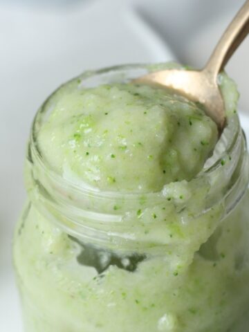 Creamy green protein smoothie in a glass jar with a spoon full of smoothie out of the jar