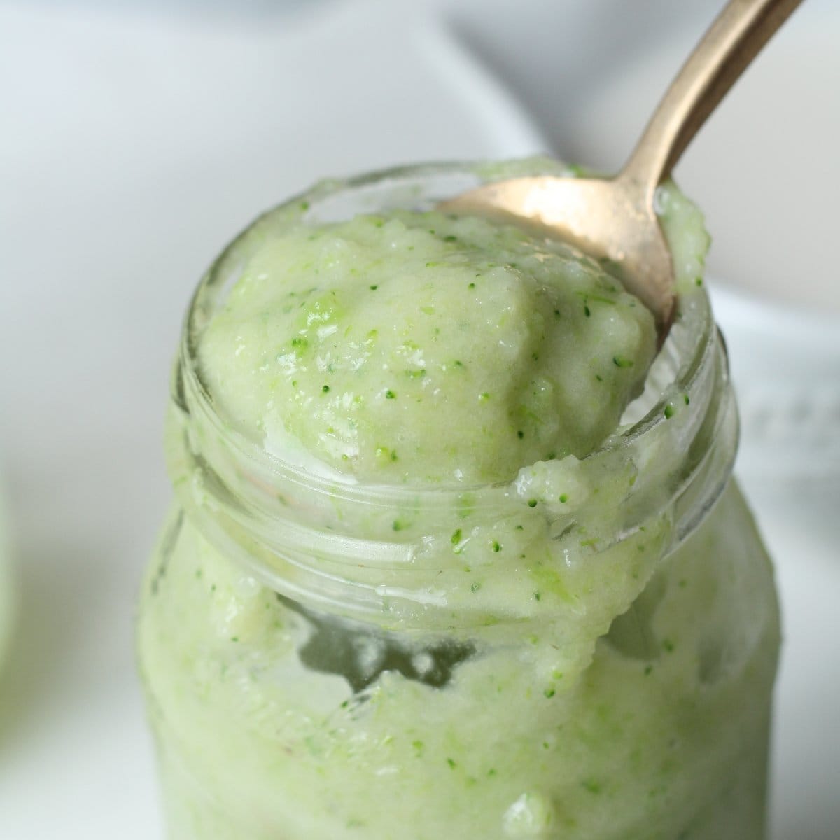 Creamy green protein smoothie in a glass jar with a spoon full of smoothie out of the jar