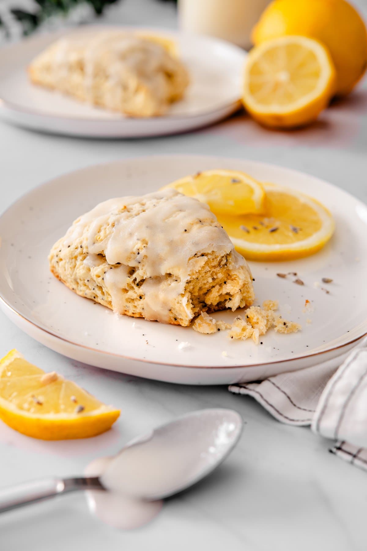 Vegan lemon poppy seed scones with lavender icing inside, served on a plate with lemon wedges and a spoon next to it.