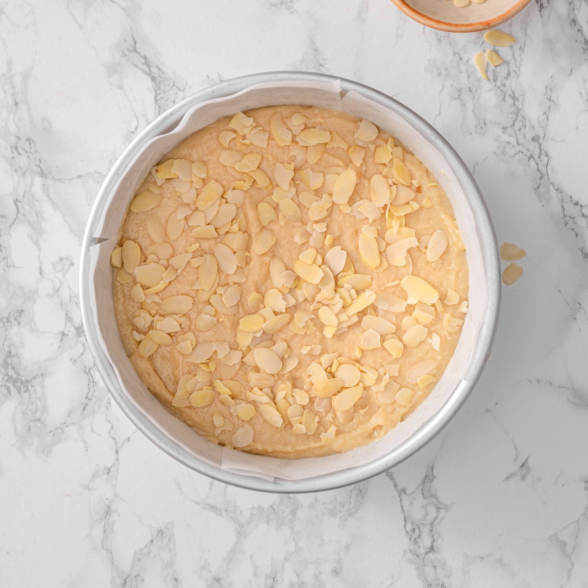 almond ricotta cake batter in a round baking dish topped with sliced almonds ready to be baked.