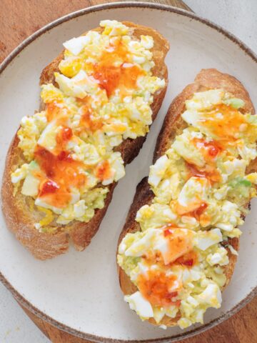 Avocado Cottage Cheese Toast on a white plate drizzled with hot sauce