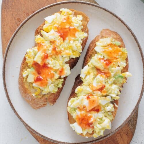 Avocado Cottage Cheese Toast on a white plate drizzled with hot sauce
