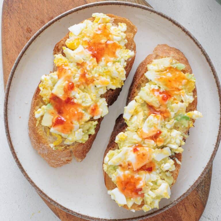 Avocado Cottage Cheese Toast on a white plate drizzled with hot sauce