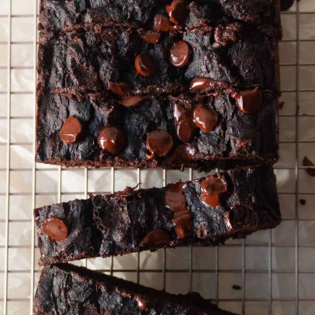 Sliced chocolate bread on a wire rack with melty chocolate chips on a dark fudgy crumb, overhead view