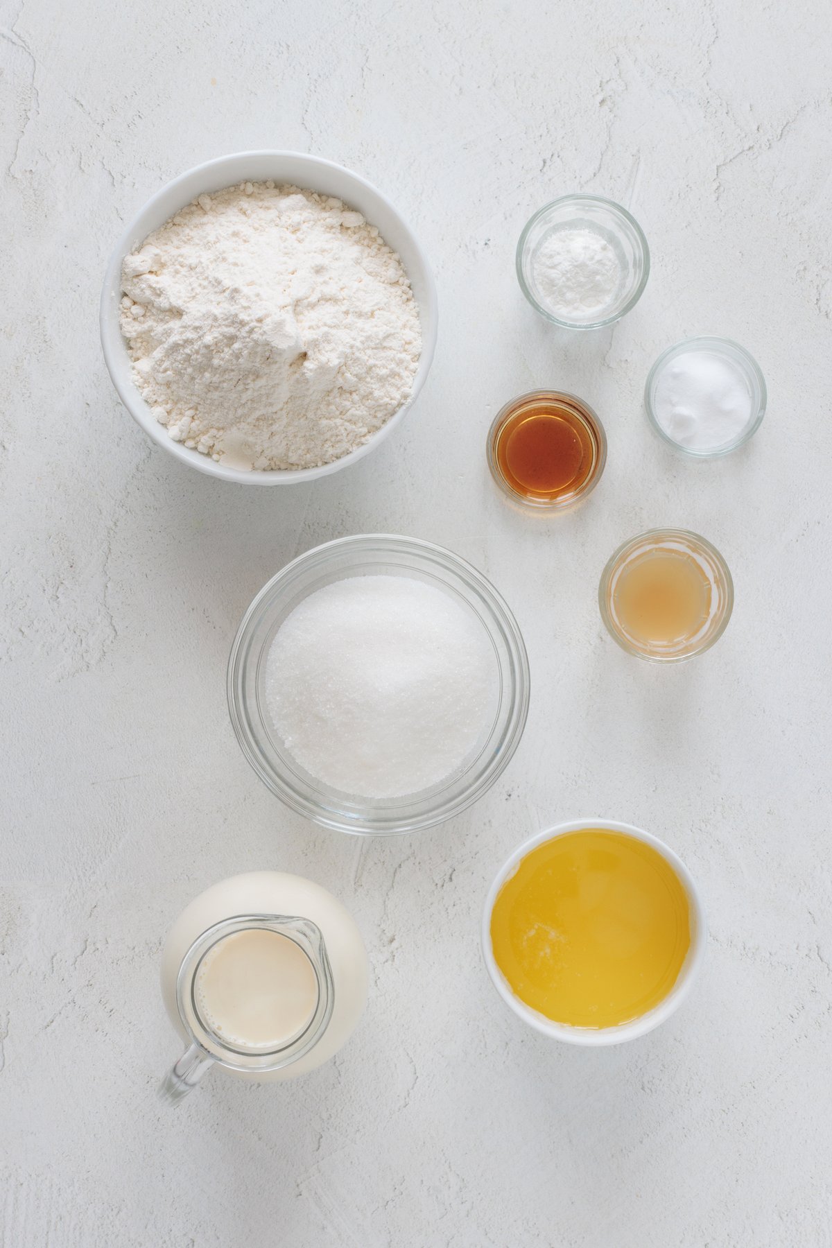 Lay out the ingredients for vegan cake pops flat: all-purpose flour, granulated sugar, baking powder, white vinegar, vanilla extract, vegetable milk on a white background