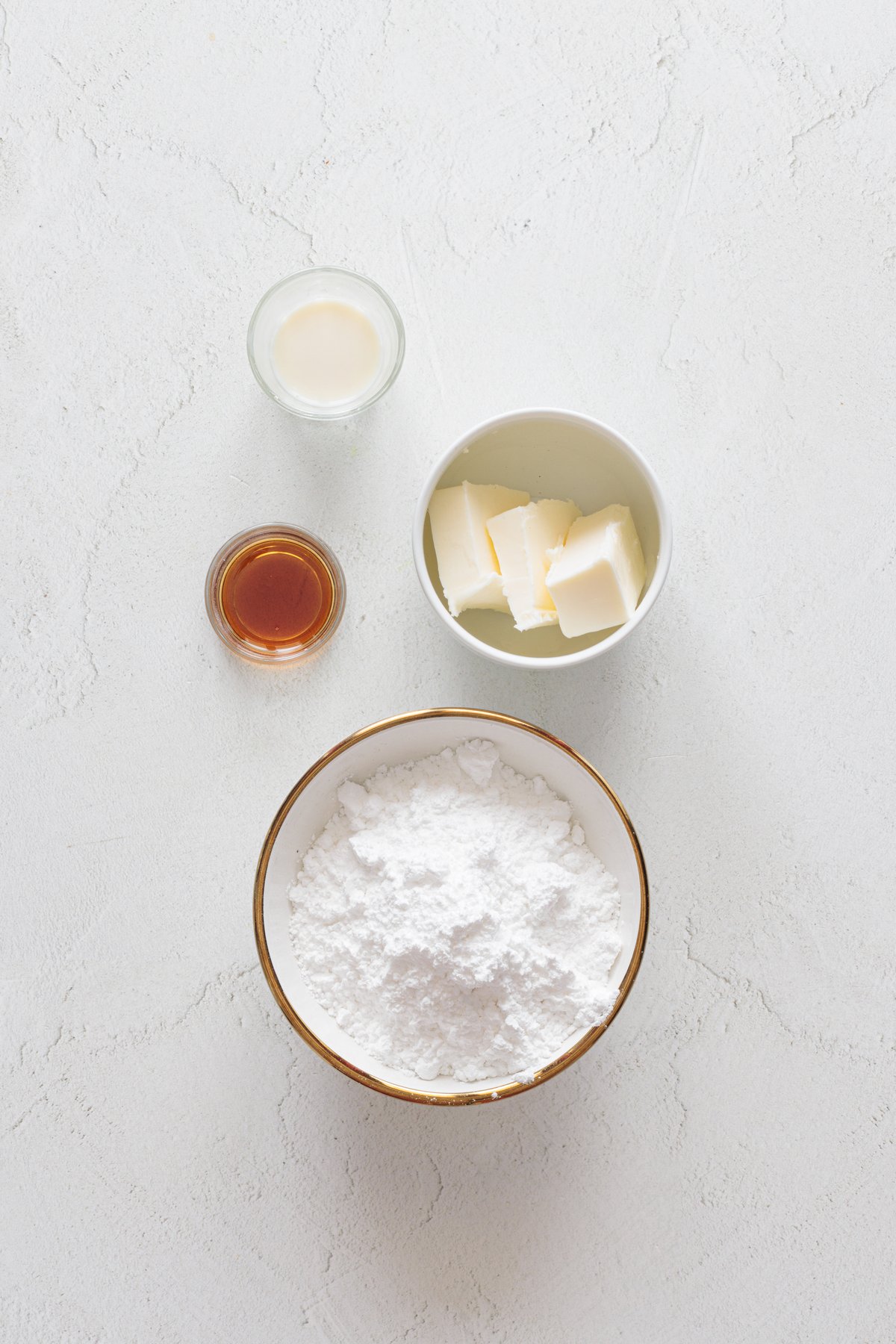 Vegan cake pop frosting ingredients: powdered sugar, vegan butter cubes, plant-based milk, and vanilla extract are displayed on a white surface.