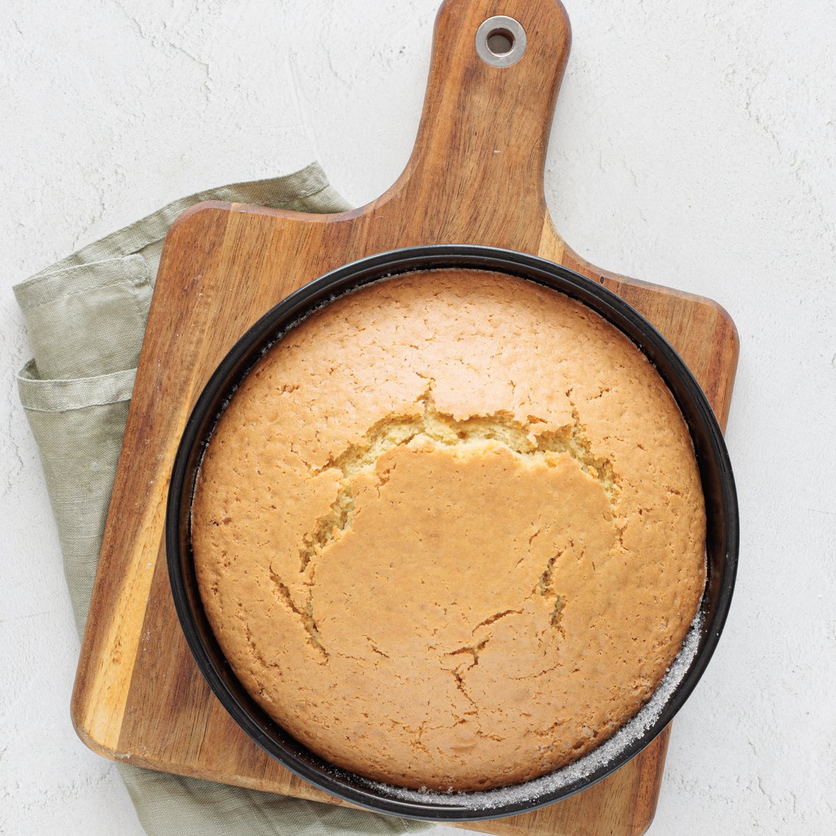 Vegan cake baked in rounds, cooled in a dark pan on a wooden serving board with a sage green linen napkin
