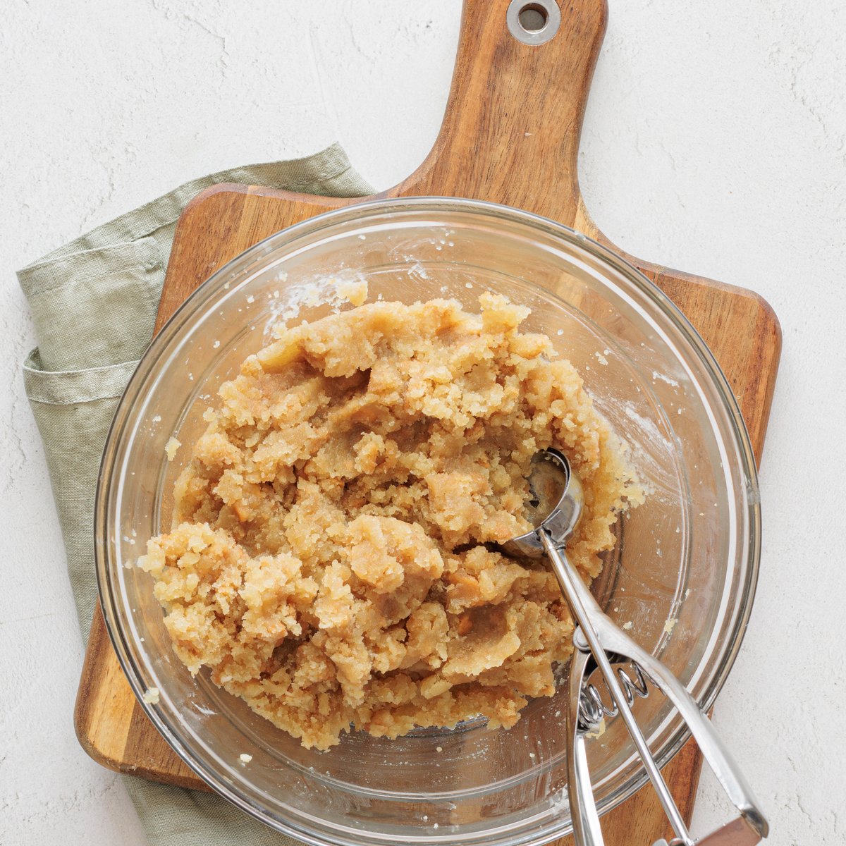 Cookie dough-like vegan cake pop mixture in a glass bowl with a cookie scoop on a wooden cutting board