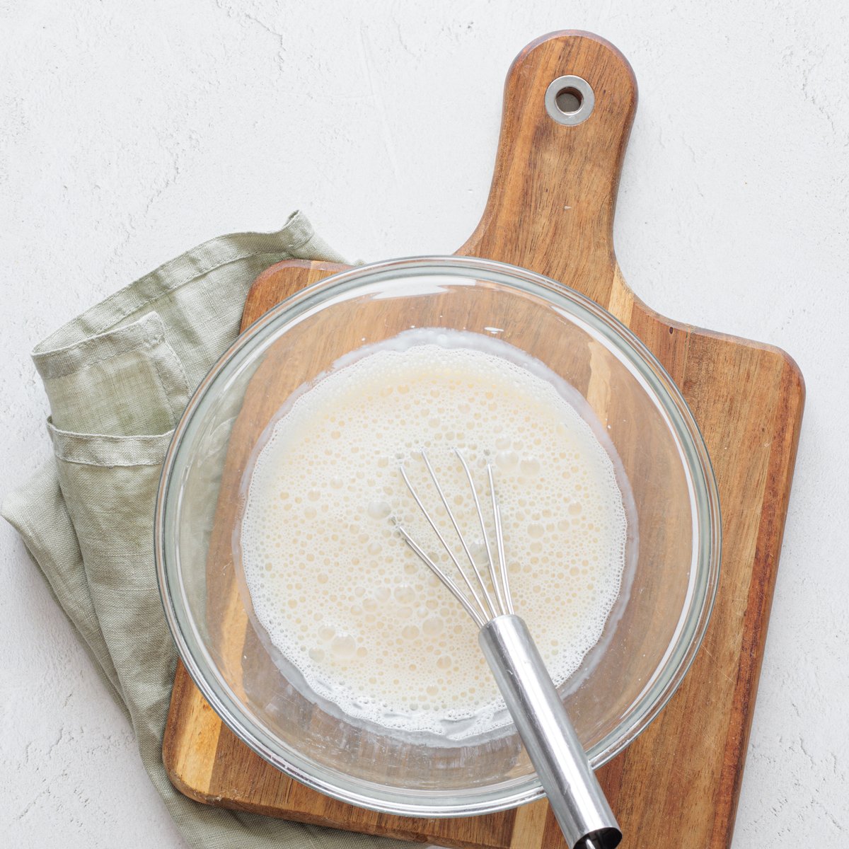 Mixture of unsweetened vegetable milk and white vinegar whisked in a glass bowl on a wooden cutting board for vegan cake pops