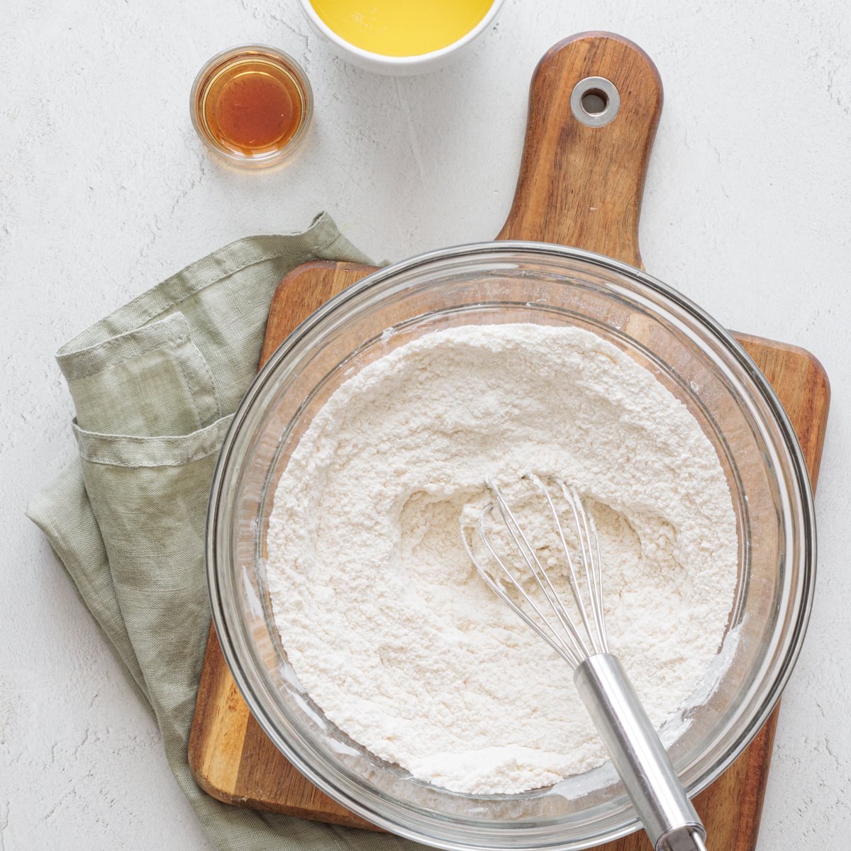 Mix all-purpose flour in a glass bowl on a wooden board. Keep melted vegan butter and vanilla extract for vegan cake pops nearby.