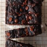 Sliced chocolate loaf cake on a wire cooling rack topped with glossy melted chocolate chips and a dense fudgy crumb