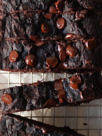 Sliced chocolate loaf cake on a wire cooling rack topped with glossy melted chocolate chips and a dense fudgy crumb