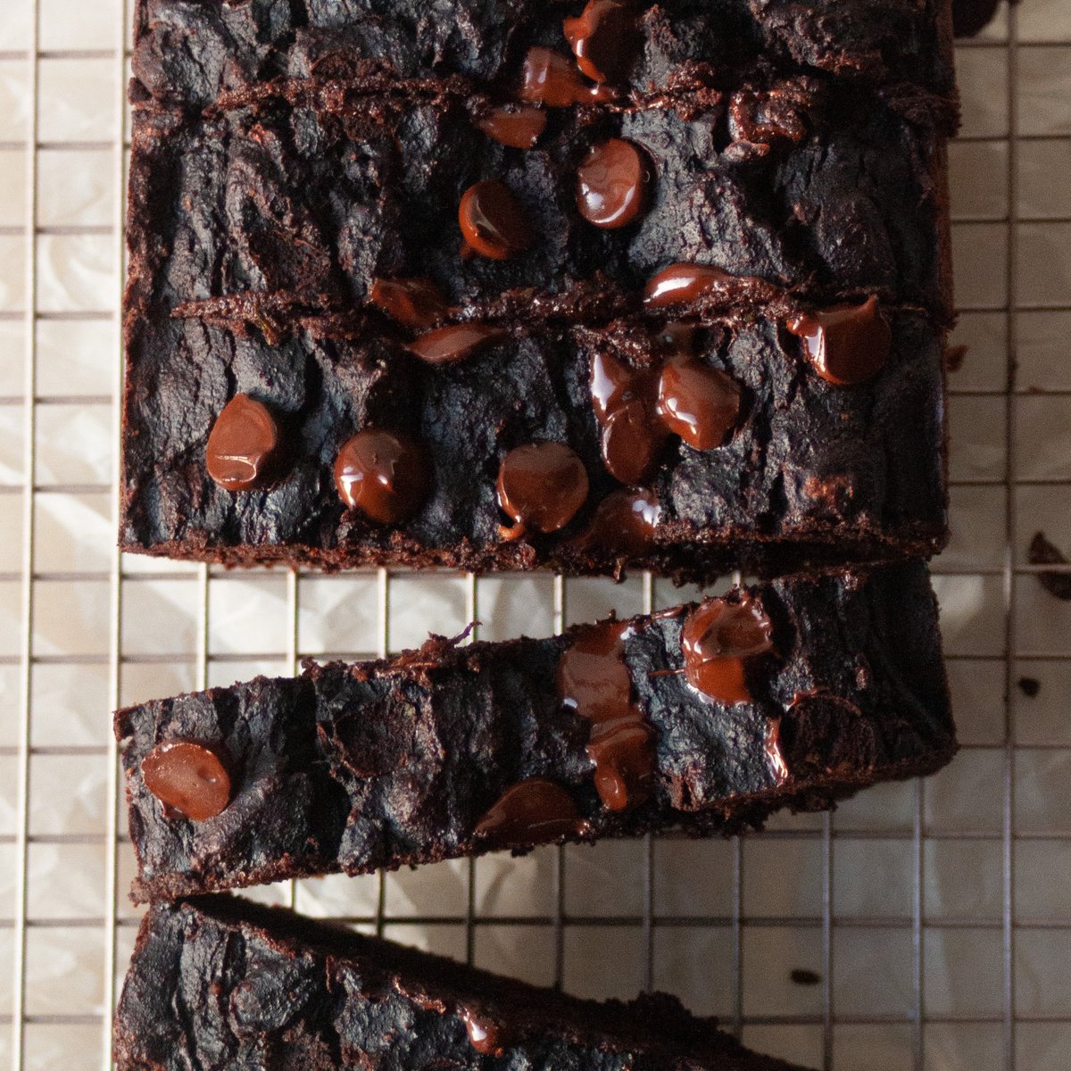 Sliced chocolate loaf cake on a wire cooling rack topped with glossy melted chocolate chips and a dense fudgy crumb