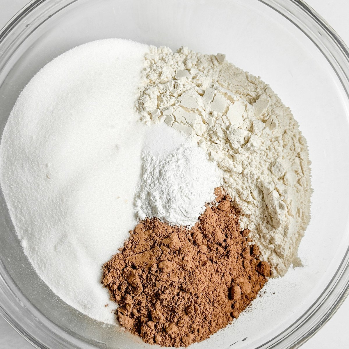 Dry ingredients for chocolate loaf cake in a glass bowl: white sugar, flour, cocoa powder, and baking powder unmixed