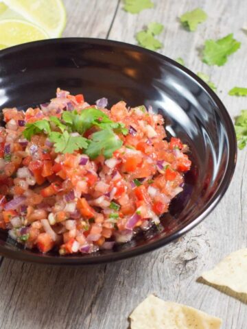 homemade salsa in a black bowl with some tortilla chips around it