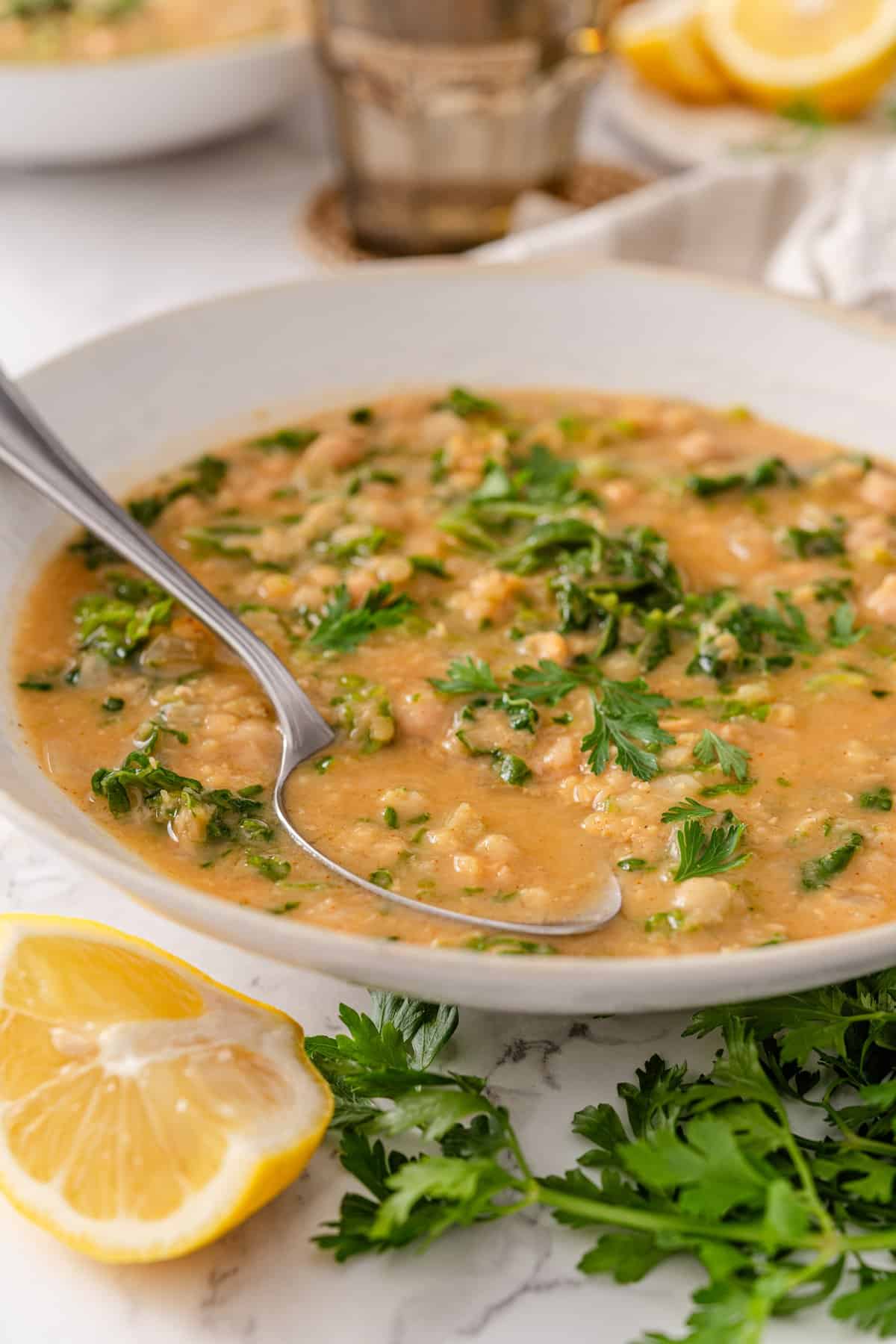 Chickpea lentil soup in a white bowl with red lentils, chickpeas, chopped kale, and fresh parsley, served with lemon wedges and a spoon.
