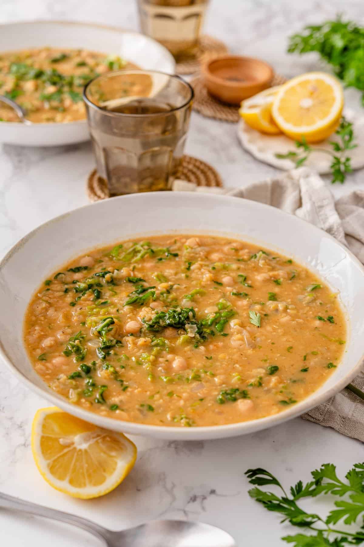 Chickpea Lentil Soup in a white bowl with red lentils, chickpeas, chopped kale, and fresh parsley, served with lemon wedges on marble