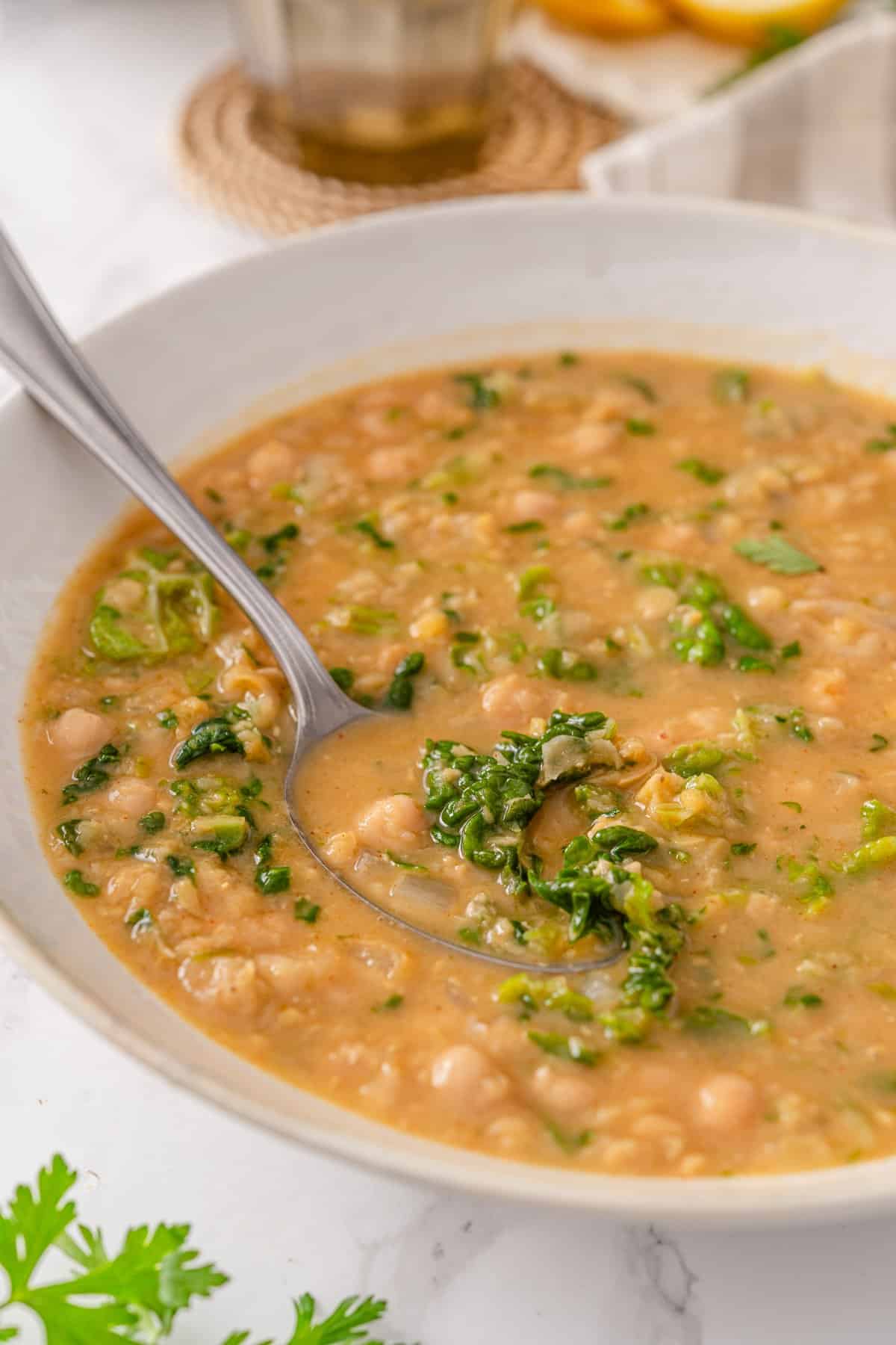 Chickpea lentil soup in a white bowl with red lentils, chickpeas, and chopped kale in a golden broth, served with a spoon.