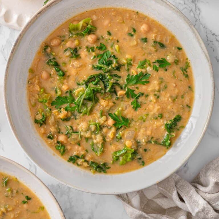 Chickpea lentil soup in a rustic white ceramic bowl with red lentils, chickpeas, chopped kale, and fresh parsley on marble